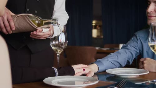Couple Celebrating with Wine Poured in Glasses by Waiter in Restaurant