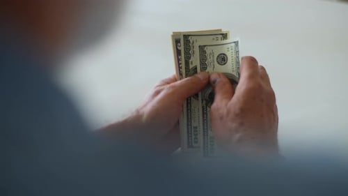 Closeup View From Back of Unrecognizable Senior Male with Wrinkled Hands Counting Dollar Bills