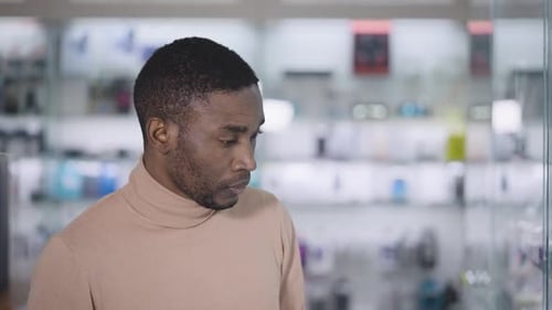 An African Man Walks Along the Glowing Windows in an Electronics Store