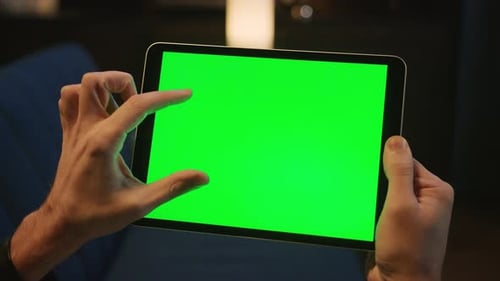 Closeup Footage of Unrecognizable Man Sitting on Sofa and Using Blank Large Green Screen Tablet in