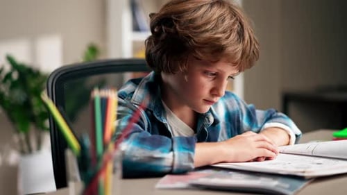 Close Up in the Children's Room a Schoolboy in a White Sweater and a Blue Checkered Shirt at a Desk