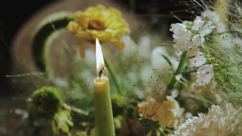 Candle Flame Burns Surrounded by Floral Arrangement