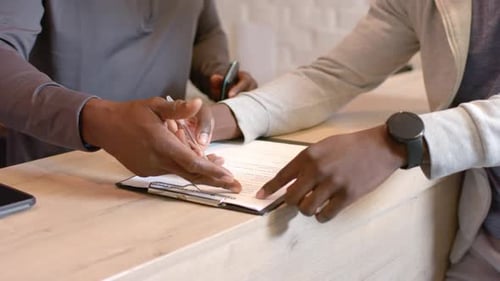 African American advisor and client finalizing form on clipboard with pen at counter after guidance