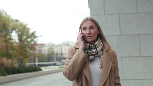 A Woman Talks on Her Phone While Enjoying a Walk in the City on a Cool Day in Autumn
