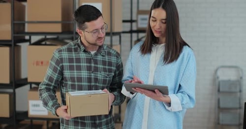 A Female Sales Manager Using a Tablet Computer is Talking to a Male Worker Holding a Cardboard