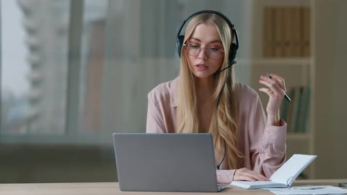 Caucasian Business Woman Talking Video Call Writing Notes Wearing Headset in Office Businesswoman