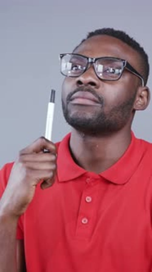 Nachdenklicher junger afroamerikanischer Mann mit nerdiger Brille in einem Brainstorming-Prozess hält Marker