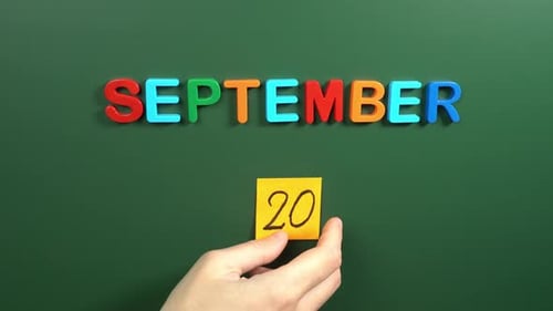 Hand sticking a sticker 20 September calendar day on school board. 20 date of September. Twentieth
