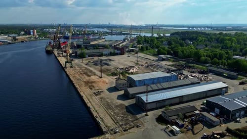 A View of an Industrial Port with Cranes, Warehouses, and Ships Along a Waterway - Aerial Drone Shot