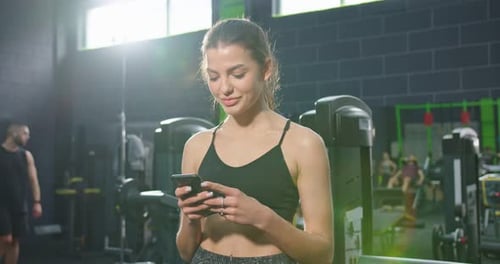 Low Angle View of the Strong Sportswoman Looking at the Smartphone Screen and Messaging with