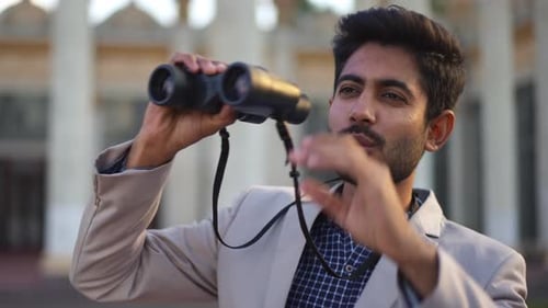 Curios Middle Eastern Young Man Looking Away Using Binoculars Standing on Urban City Street