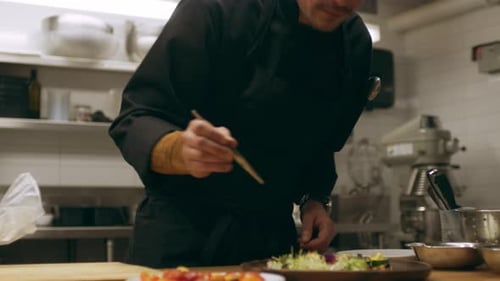Professional chef garnishing salad with herbs in restaurant kitchen