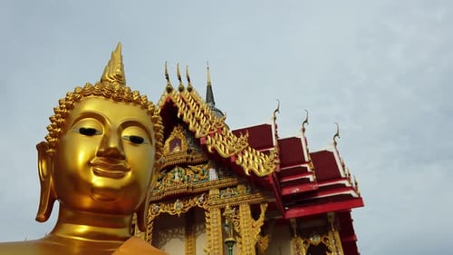 Dolly out shot of a golden Buddha statue and Thai Buddhist Temple with ornate style of high gables,