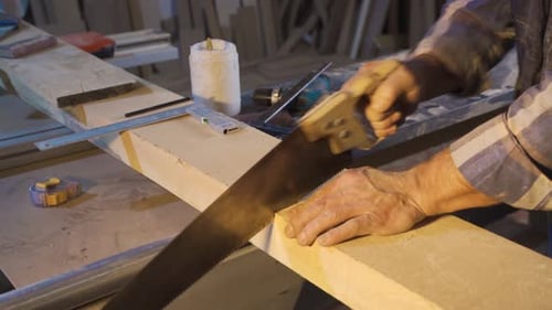 Close-up carpenter is cutting wood with a handsaw.