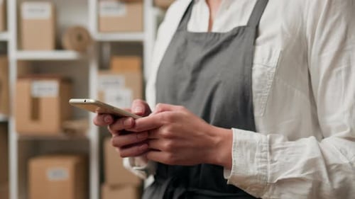 Entrepôt industriel, femme d'affaires tenant joyeusement un smartphone dans la salle de commerce électronique