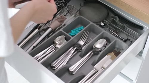 Cutlery drawer in a modern kitchen reveals organized utensils, reaching for a spoon, highlighting th