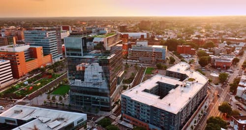 Approaching modern glass building with green zone on top. Philadelphia cityscape from air at sunset.