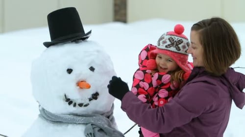 Madre e hija disfrutan construyendo juntas un muñeco de nieve en el jardín de invierno