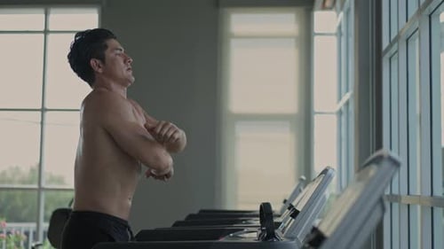 A muscular man stretching body walking on treadmill at gym