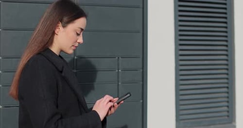 Woman Receiving Parcel From Post Terminal Machine Using Smartphone Outdoors