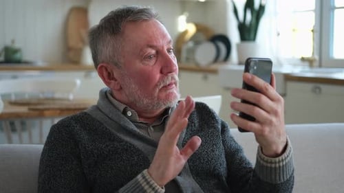 Senior Man Video Chats on Smartphone at Home