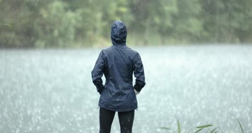 Woman Stands in the Pouring Rain Against the Background of a Lake Shot on Super Slow Motion Camera