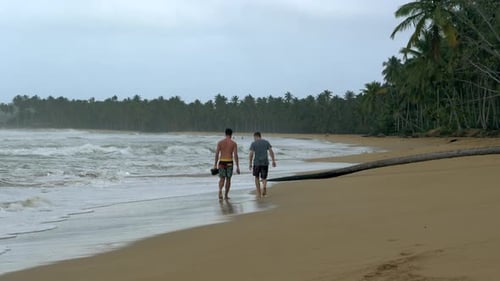 Two men leisurely walk down a Dominican beach chatting.