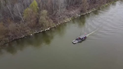 Aerial tracking shot of polish boat cruising on Vistula River during cloudy day near the shore.