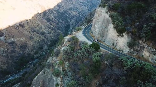 Aerial tracking 4k shot of a car speeding on mountain serpentines. River valley down below on the le