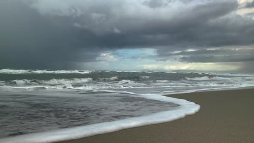 Sea waves run along the sandy shore, storm clouds in the background. Slow motion.