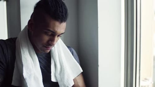 Young man with dreadlocks texts on smartphone resting after gym workout