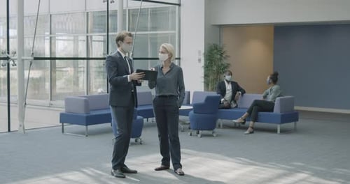 Business man meeting in office lobby wearing protective face mask using digital tablet technology