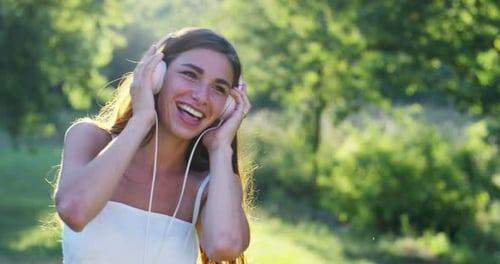 Eine Frau im Grünen mit Kopfhörern, die Musik hört, singt, tanzt und Spaß hat mit einem