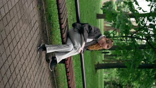 Vertical Video In the Park a Young Lonely Girl in a Black Jacket with Her Hair Pulled Together is