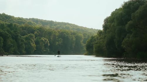 Beautiful Landscape With River In Forest And Silhouette Of Paddle Boarder Active Rest In Nature