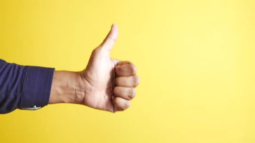 Hand Giving Thumbs Up on Yellow Background