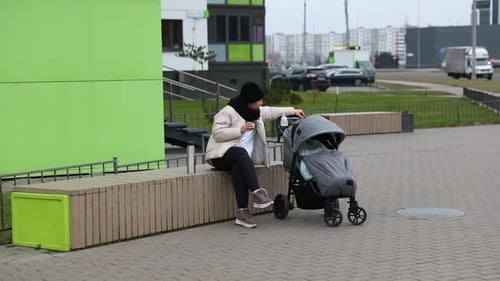 Woman Enjoying a Snack While Seated Next to a Stroller on a City Sidewalk