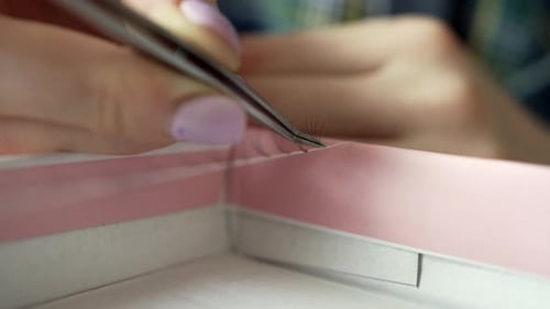 Woman Using Tweezers to Pick Up False Eyelashes