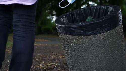 Woman dropping face mask into a bin close up shot