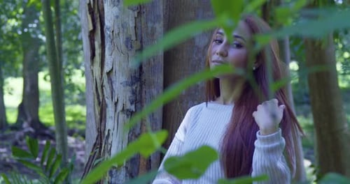 Red hair model stands in a tropical park with leaves from a tree in the foreground