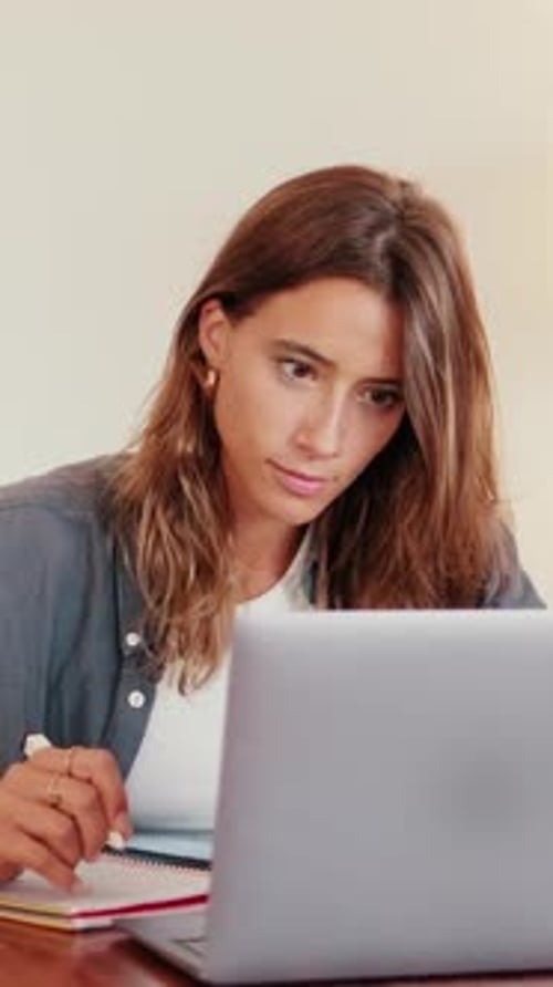 Woman with Laptop Writing in a Notebook