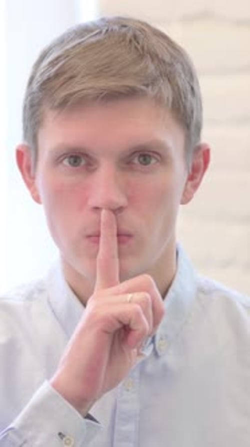 Joven empresario pidiendo silencio, dedo en los labios, vídeo vertical