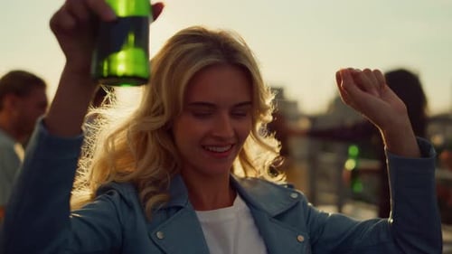Smiling woman dancing with beer at rooftop party