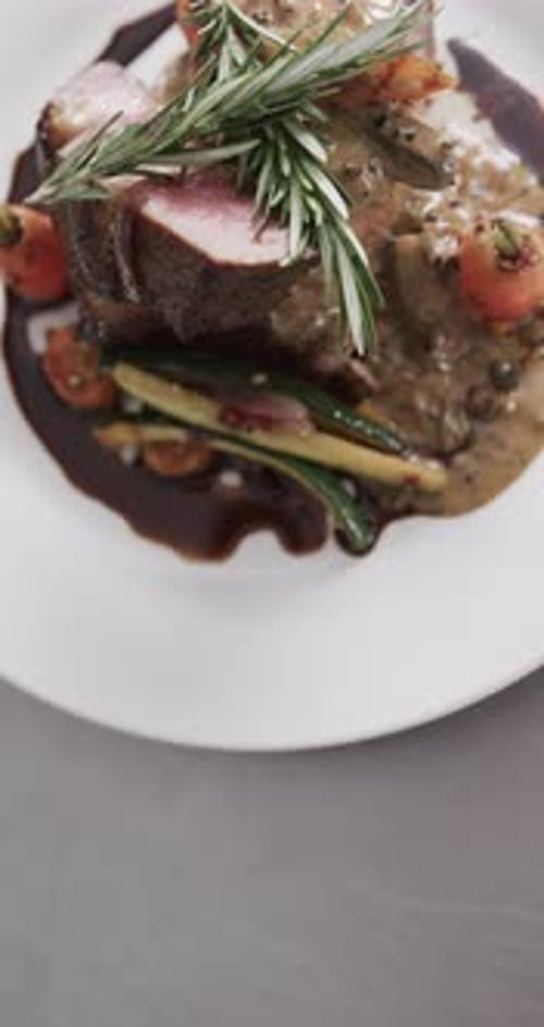 Upper view of prepared and decorated meal on white plate on in kitchen, slow motion, vertical