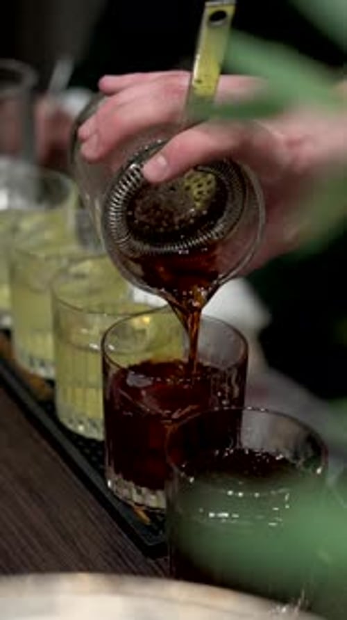 Bartender Pours Cocktail with Ice in Bar Setting