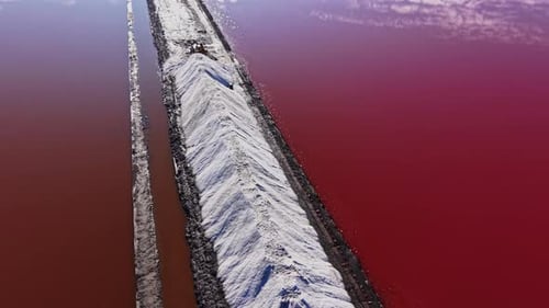 Salt piles in industrial area near red water under clear sky