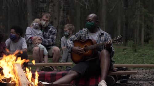 Family gathers around a campfire in a wooded area