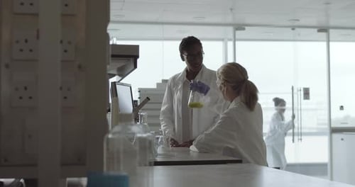 Scientists Examining Flask with Yellow Liquid in Lab