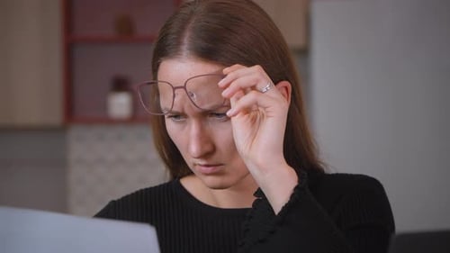 Frau arbeitet von zu Hause aus und passt die Brille an und versucht, den Laptop-Bildschirm zu lesen