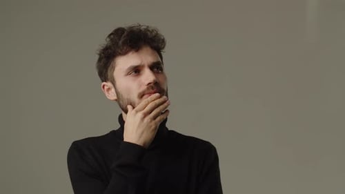 Young Man Rubbing His Beard and Thinking About Something Studio Footage of a Pensive Man Trying to